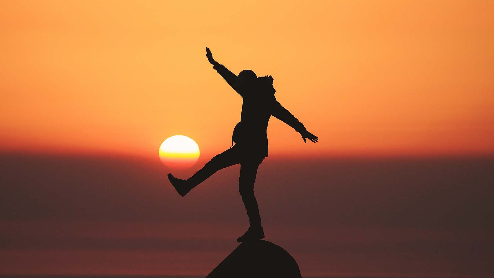 Pessoa se equilibrando em uma pedra no nascer do sol